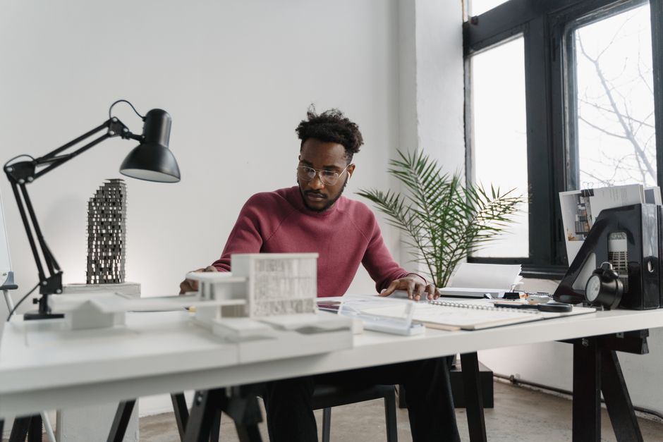 An architect seen from above, drawing precise plans on a large blueprint at a bright, minimalist wooden desk, symbolizing the careful construction of brand authority.