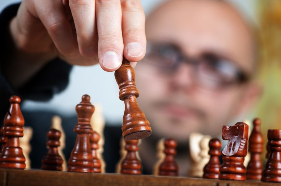 Close-up of a hand making a strategic move with a chess piece on a modern, minimalist chess board, symbolizing the new pla...