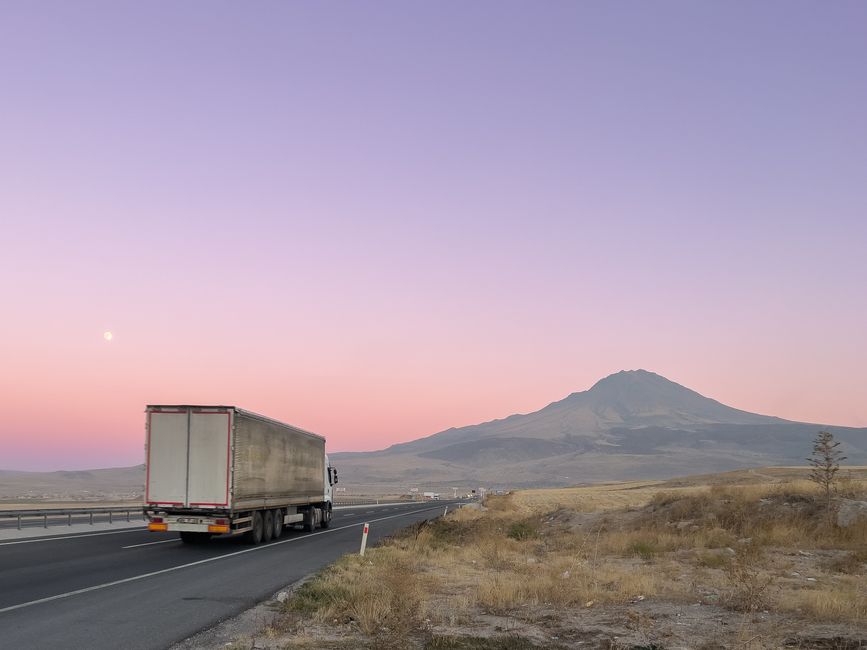 A moving van driving down a long, empty highway through a scenic landscape at sunset, representing the journey and logistics of a cross-country move.