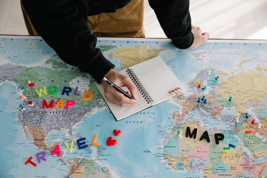 Top-down view of hands spread across a large map, planning a route with a laptop and coffee cup nearby, suggesting careful...